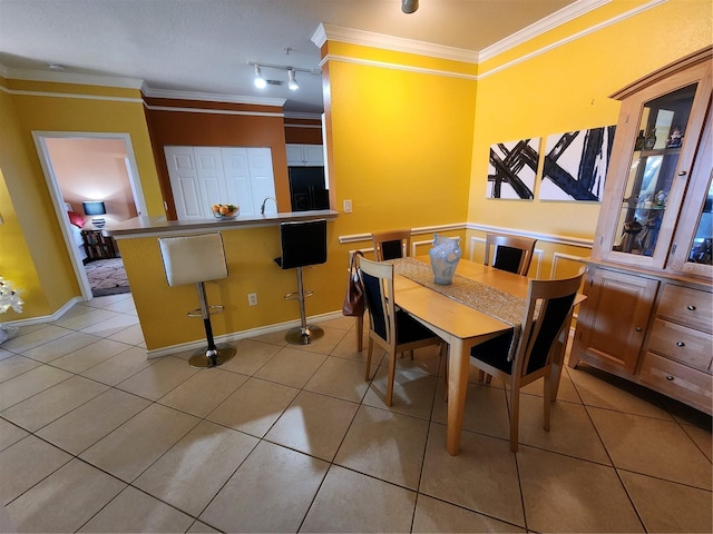 dining area with sink, light tile patterned floors, track lighting, and ornamental molding