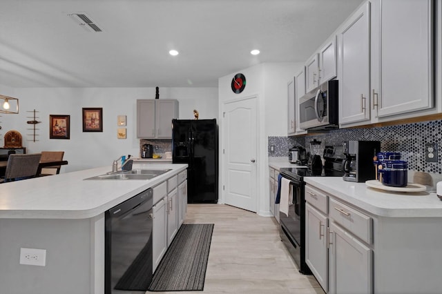 kitchen featuring black appliances, tasteful backsplash, light hardwood / wood-style floors, sink, and an island with sink