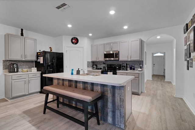 kitchen featuring black appliances, sink, gray cabinets, a kitchen island with sink, and a breakfast bar