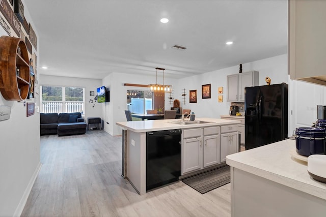 kitchen with black appliances, decorative light fixtures, sink, light wood-type flooring, and a center island with sink