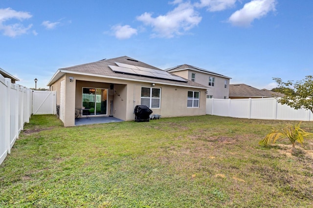 back of house featuring a patio area, a lawn, and solar panels