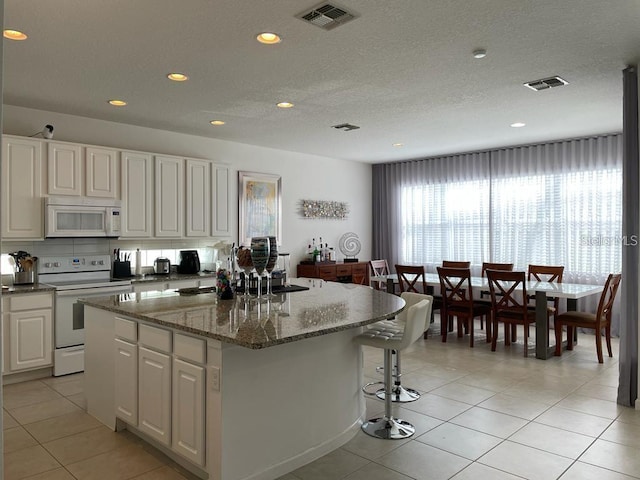 kitchen featuring white appliances, stone counters, white cabinetry, a kitchen island, and light tile patterned flooring