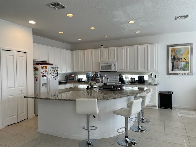 kitchen featuring a spacious island, white appliances, white cabinetry, dark stone countertops, and light tile patterned flooring