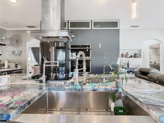 kitchen featuring high quality fridge, island range hood, hanging light fixtures, and multiple ovens