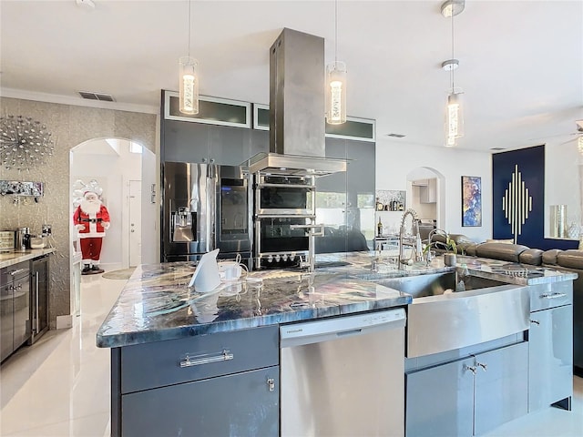 kitchen with sink, dark stone countertops, an island with sink, appliances with stainless steel finishes, and island exhaust hood