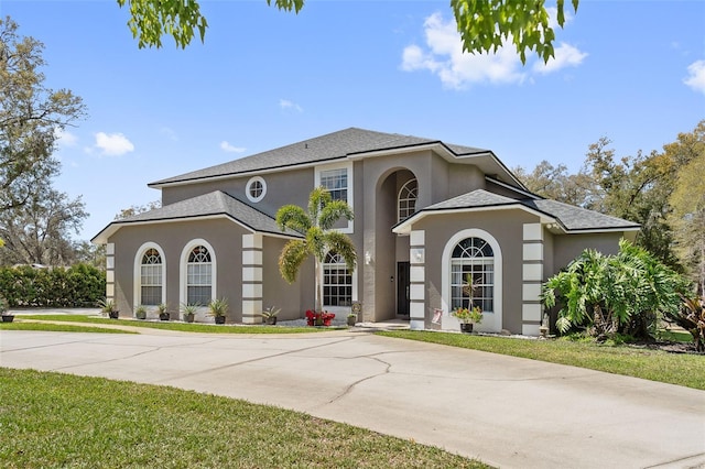 view of front facade featuring driveway, roof with shingles, a front yard, and stucco siding