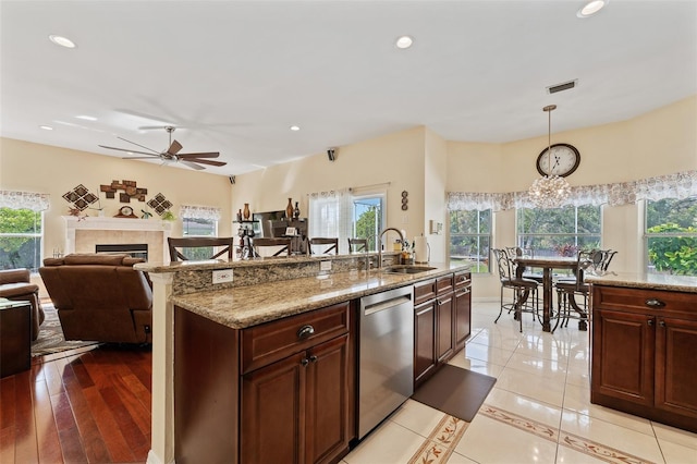 kitchen featuring light stone counters, a tile fireplace, a sink, stainless steel dishwasher, and pendant lighting