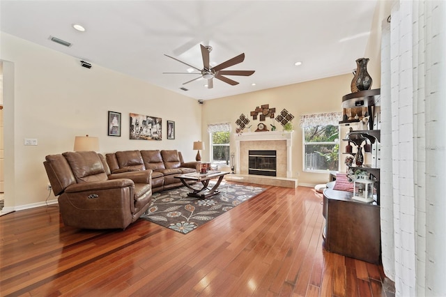 living area with a fireplace, wood-type flooring, visible vents, ceiling fan, and baseboards