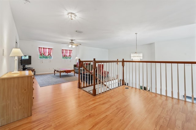 interior space with ceiling fan with notable chandelier, light wood-type flooring, visible vents, and baseboards