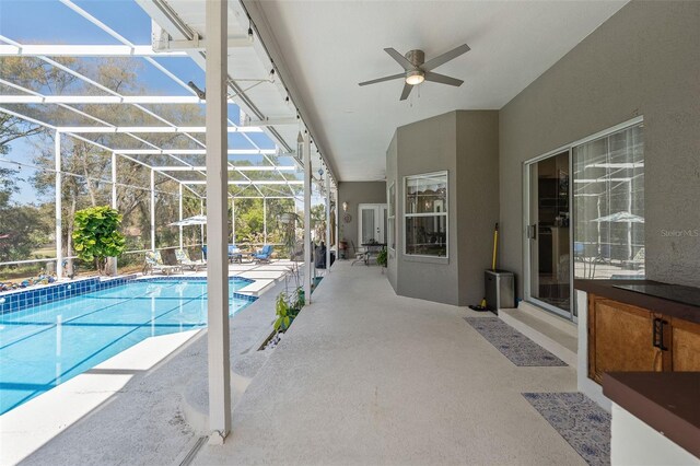 outdoor pool with glass enclosure, a ceiling fan, and a patio