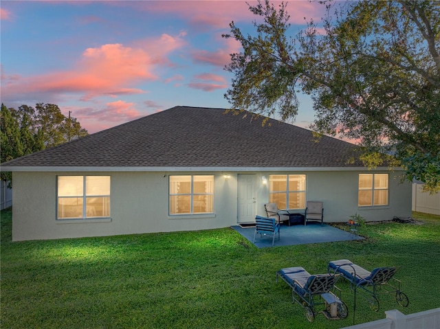 back house at dusk with a lawn and a patio