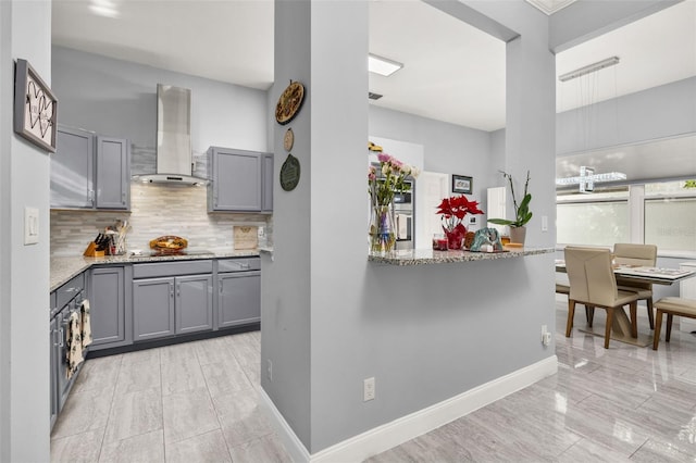 kitchen with cooktop, backsplash, gray cabinets, and wall chimney range hood