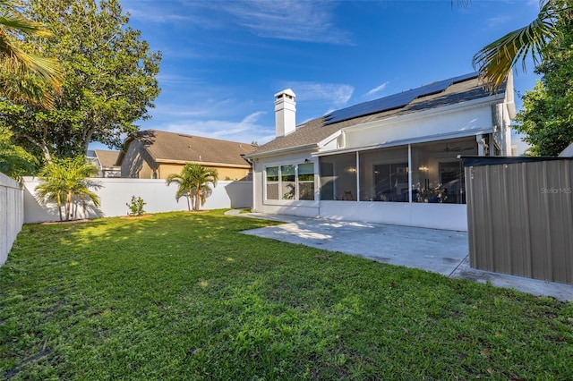 rear view of property featuring a lawn, a patio area, a sunroom, and solar panels