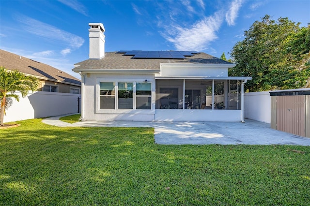 rear view of house featuring a lawn, a patio area, a sunroom, and solar panels