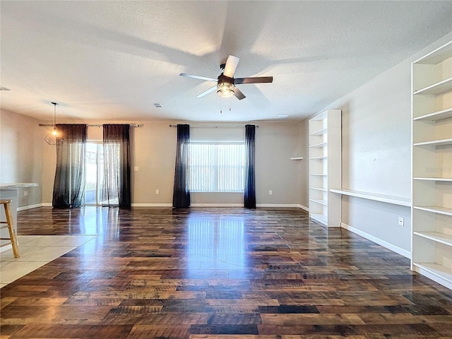 spare room featuring a textured ceiling, ceiling fan with notable chandelier, a healthy amount of sunlight, and dark wood-type flooring