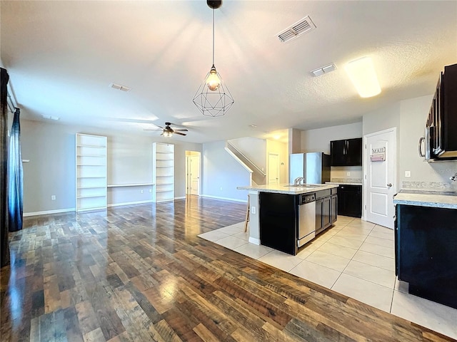 kitchen with appliances with stainless steel finishes, a breakfast bar, ceiling fan, hanging light fixtures, and an island with sink