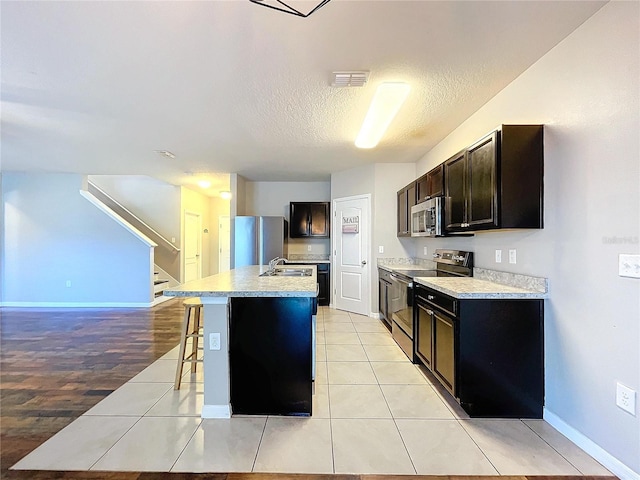 kitchen featuring light tile patterned floors, stainless steel appliances, a kitchen island with sink, and a breakfast bar area