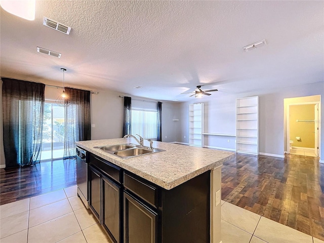 kitchen with stainless steel dishwasher, a textured ceiling, a kitchen island with sink, sink, and decorative light fixtures