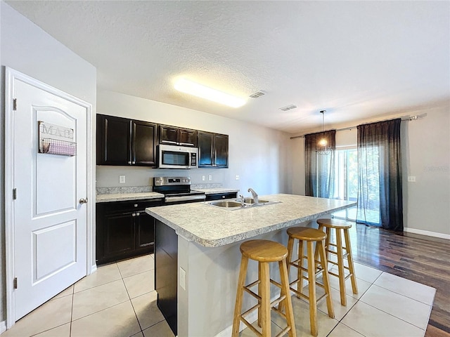 kitchen with sink, pendant lighting, a textured ceiling, a center island with sink, and appliances with stainless steel finishes