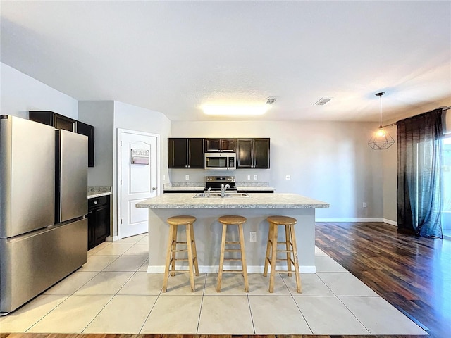 kitchen with a breakfast bar, stainless steel appliances, sink, decorative light fixtures, and a center island with sink