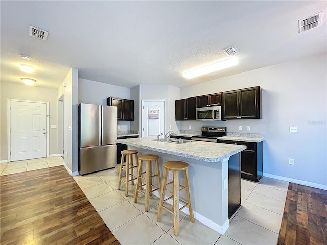 kitchen with dark brown cabinetry, light tile patterned flooring, an island with sink, and appliances with stainless steel finishes