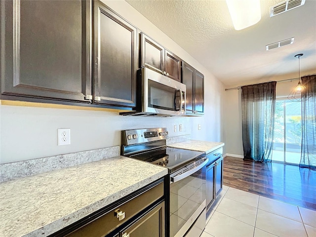 kitchen featuring a textured ceiling, appliances with stainless steel finishes, decorative light fixtures, light tile patterned flooring, and dark brown cabinets