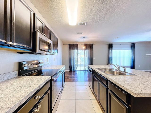 kitchen with appliances with stainless steel finishes, a kitchen island with sink, sink, hanging light fixtures, and light tile patterned flooring