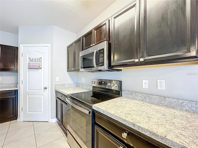 kitchen with dark brown cabinetry, light tile patterned floors, stainless steel appliances, and a textured ceiling