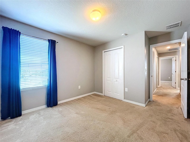 unfurnished bedroom with a textured ceiling, light carpet, and a closet