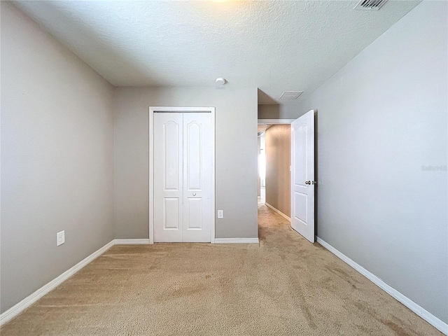 unfurnished bedroom featuring a closet, light colored carpet, and a textured ceiling