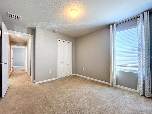 unfurnished bedroom featuring light carpet, a textured ceiling, and a closet