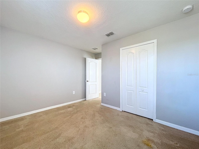 unfurnished bedroom featuring a textured ceiling, light colored carpet, and a closet