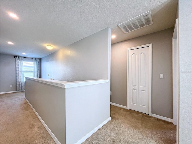 corridor with a textured ceiling and light carpet