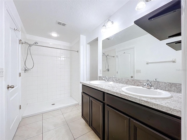 bathroom featuring a tile shower, tile patterned flooring, vanity, and a textured ceiling