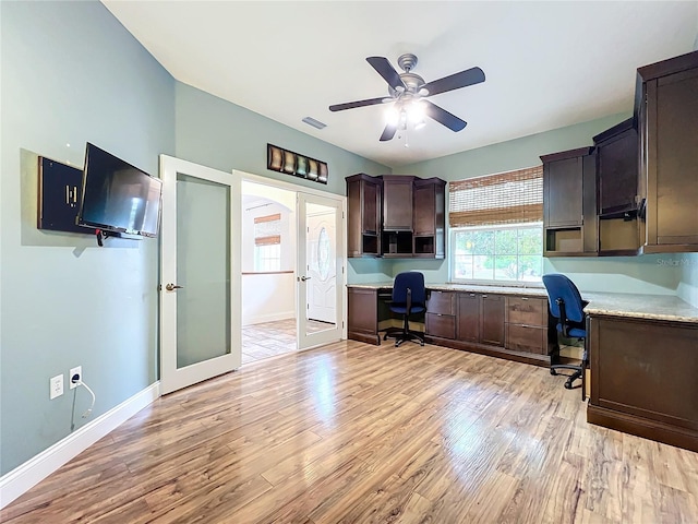 unfurnished office featuring ceiling fan, built in desk, french doors, and light hardwood / wood-style flooring