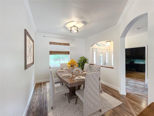 dining space featuring wood-type flooring, a textured ceiling, and ornamental molding