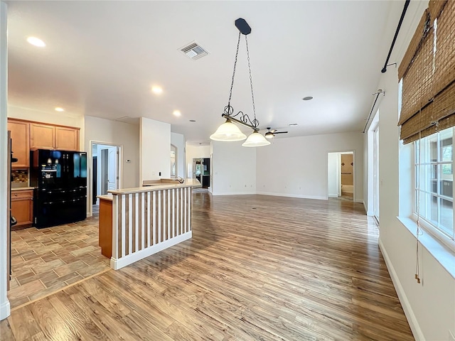 kitchen with hanging light fixtures, black fridge with ice dispenser, a kitchen island, and light hardwood / wood-style floors