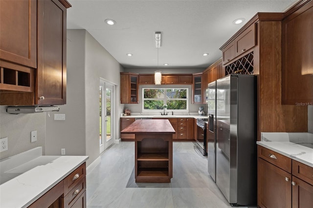 kitchen featuring light stone countertops, hanging light fixtures, stainless steel appliances, and sink