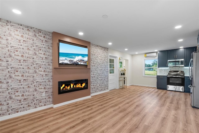 unfurnished living room with a wall mounted air conditioner, a large fireplace, and light hardwood / wood-style flooring