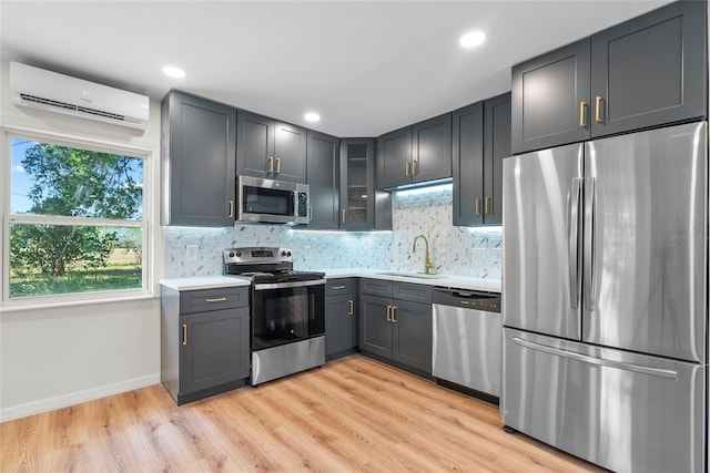 kitchen featuring sink, stainless steel appliances, a wall unit AC, and light hardwood / wood-style flooring