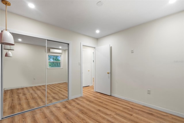 unfurnished bedroom featuring light hardwood / wood-style floors, an AC wall unit, and a closet