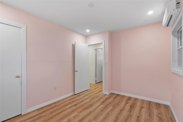 unfurnished bedroom with a wall mounted AC and light hardwood / wood-style flooring