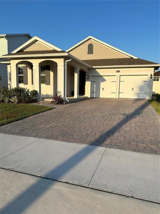 ranch-style house with a garage, decorative driveway, and stucco siding