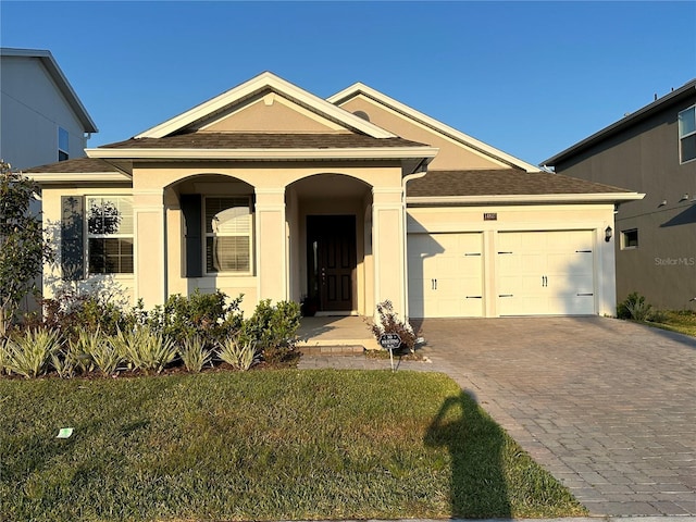 view of front of property featuring a garage, decorative driveway, a front yard, and stucco siding