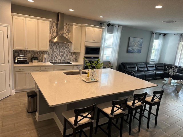 kitchen with open floor plan, light countertops, wall chimney range hood, white cabinetry, and a sink