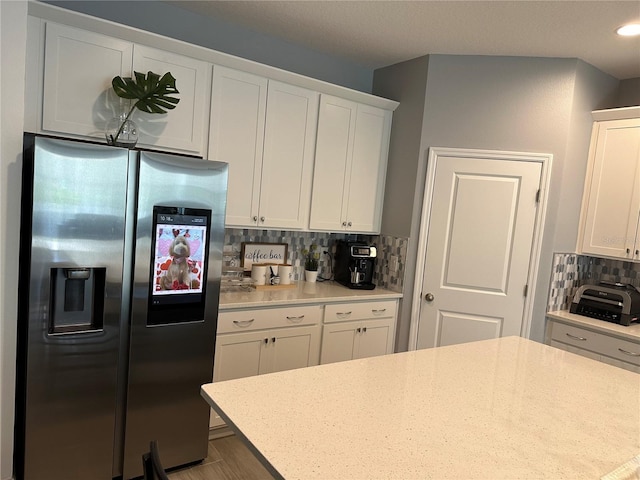 kitchen featuring tasteful backsplash, white cabinetry, light stone counters, and stainless steel fridge with ice dispenser