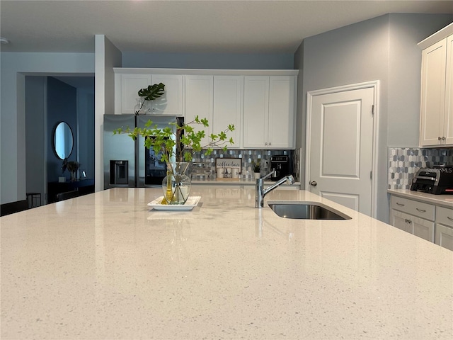 kitchen featuring light stone countertops, stainless steel fridge, white cabinets, and a sink