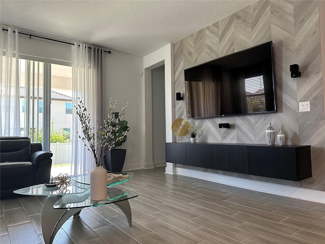 living area with wood tiled floor, an accent wall, baseboards, and a textured ceiling