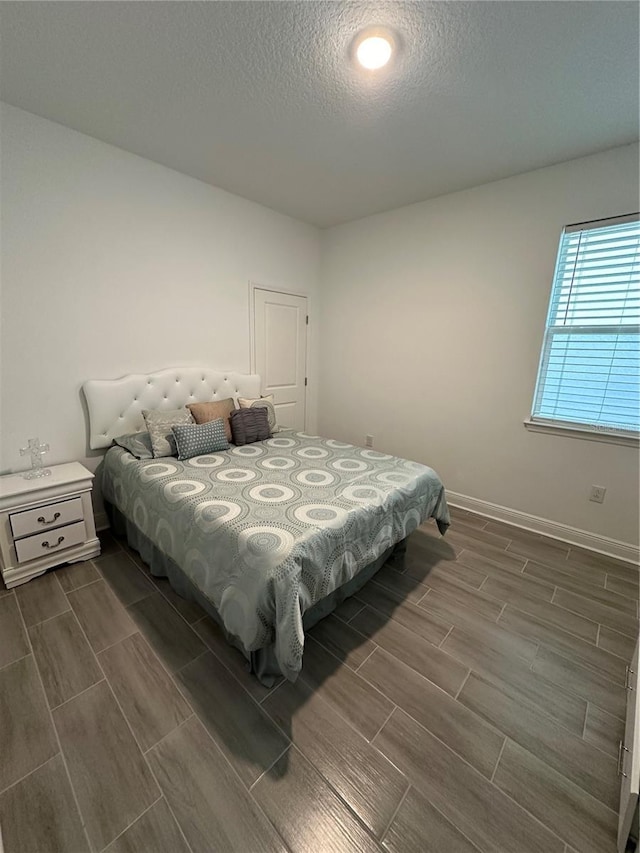 bedroom with baseboards, a textured ceiling, and wood tiled floor