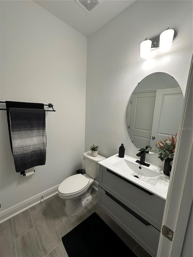 bathroom with toilet, vanity, visible vents, and baseboards